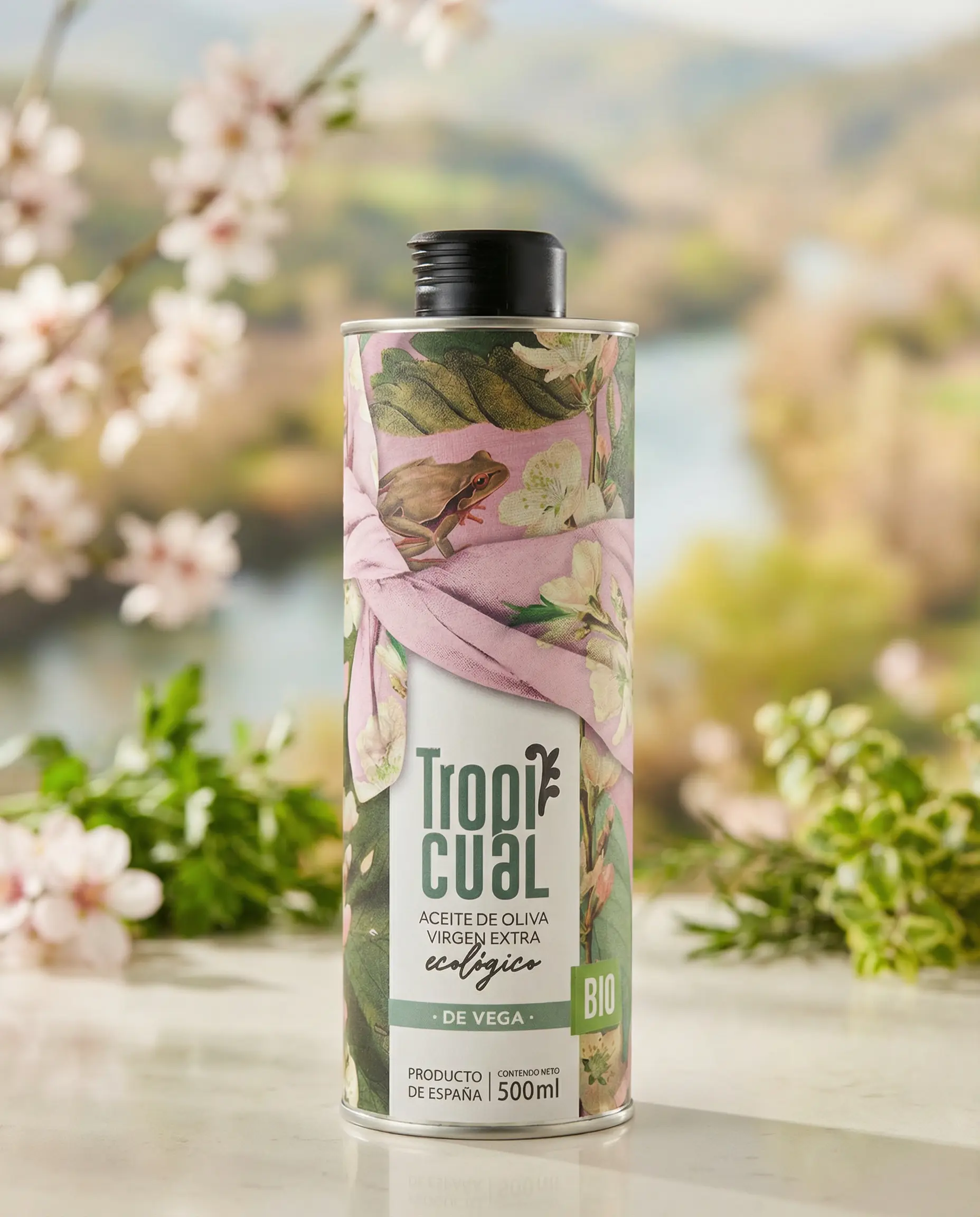 tropicual-de-vega-bio-olivenoel-500ml-design Tropicual de Vega Bio-Olivenöl in der 500ml Dose, präsentiert auf einem hellen Steintisch vor einem weichgezeichneten Hintergrund mit blühenden Mandelbäumen und mediterraner Landschaft.